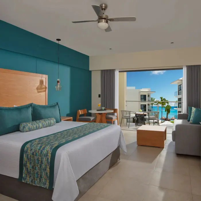 Ocean view suite featuring king bed, lounge space, and balcony with seating and vibrant sea views.