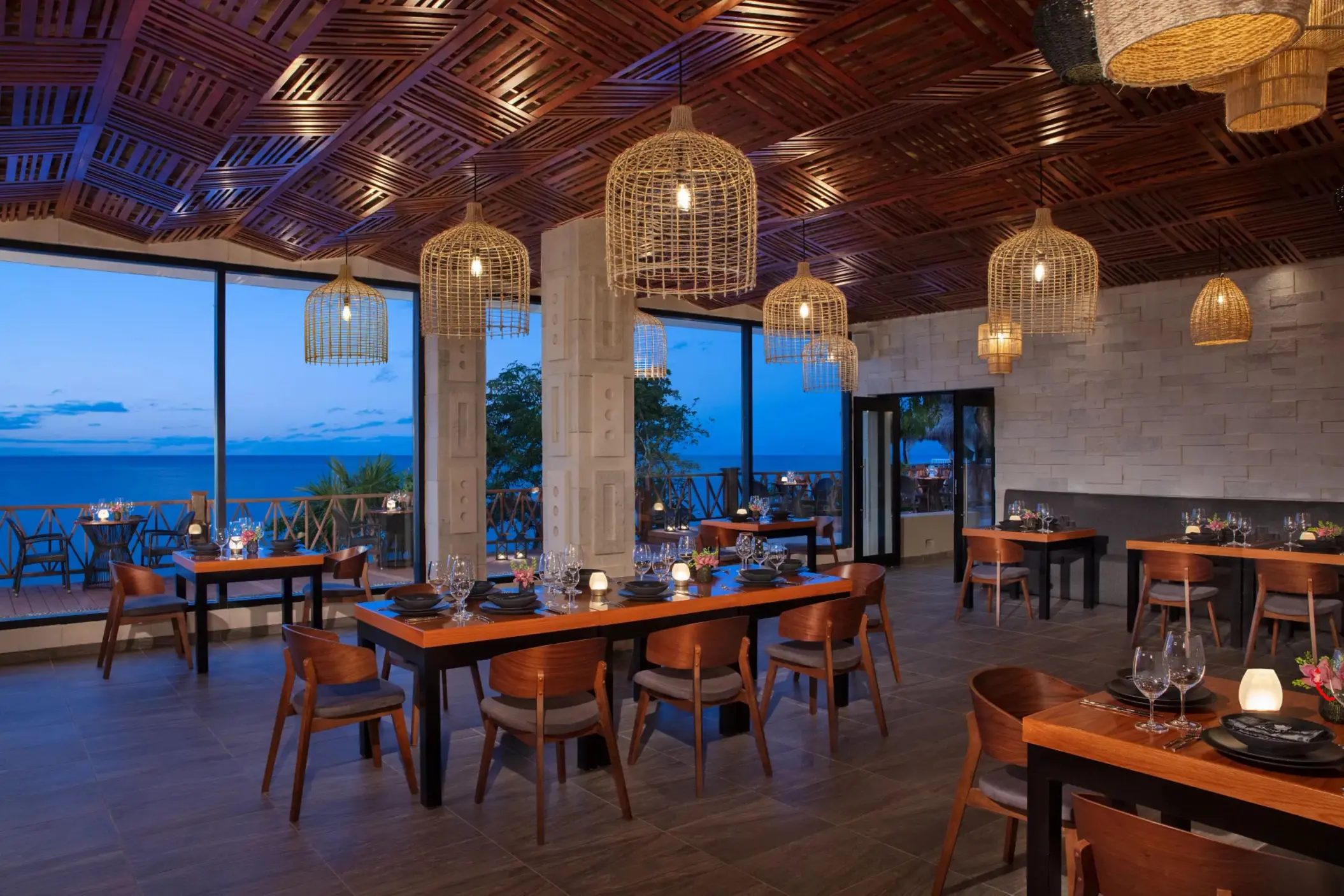 Elegant open-air restaurant with ocean views, modern wood ceiling, and cozy lighting at dusk.