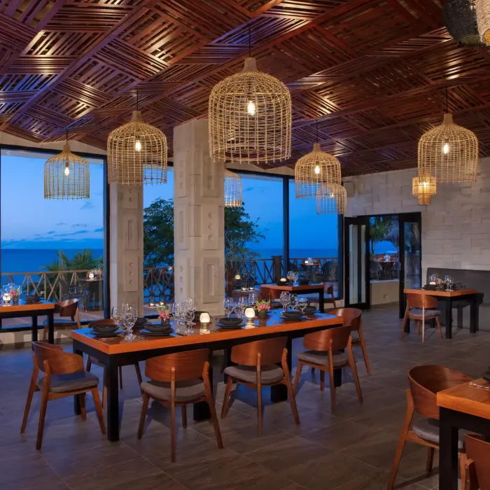 Elegant open-air restaurant with ocean views, modern wood ceiling, and cozy lighting at dusk.