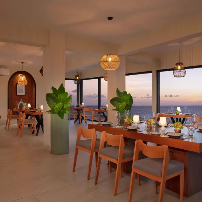 Chic indoor dining at Olio restaurant with soft lighting, ocean views, and stylish wooden furnishings.