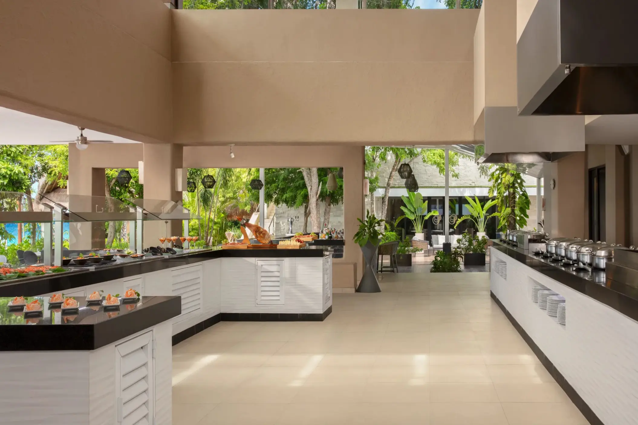 Spacious buffet setup at World Café with modern counters, tropical plants, and daylight-filled dining area.