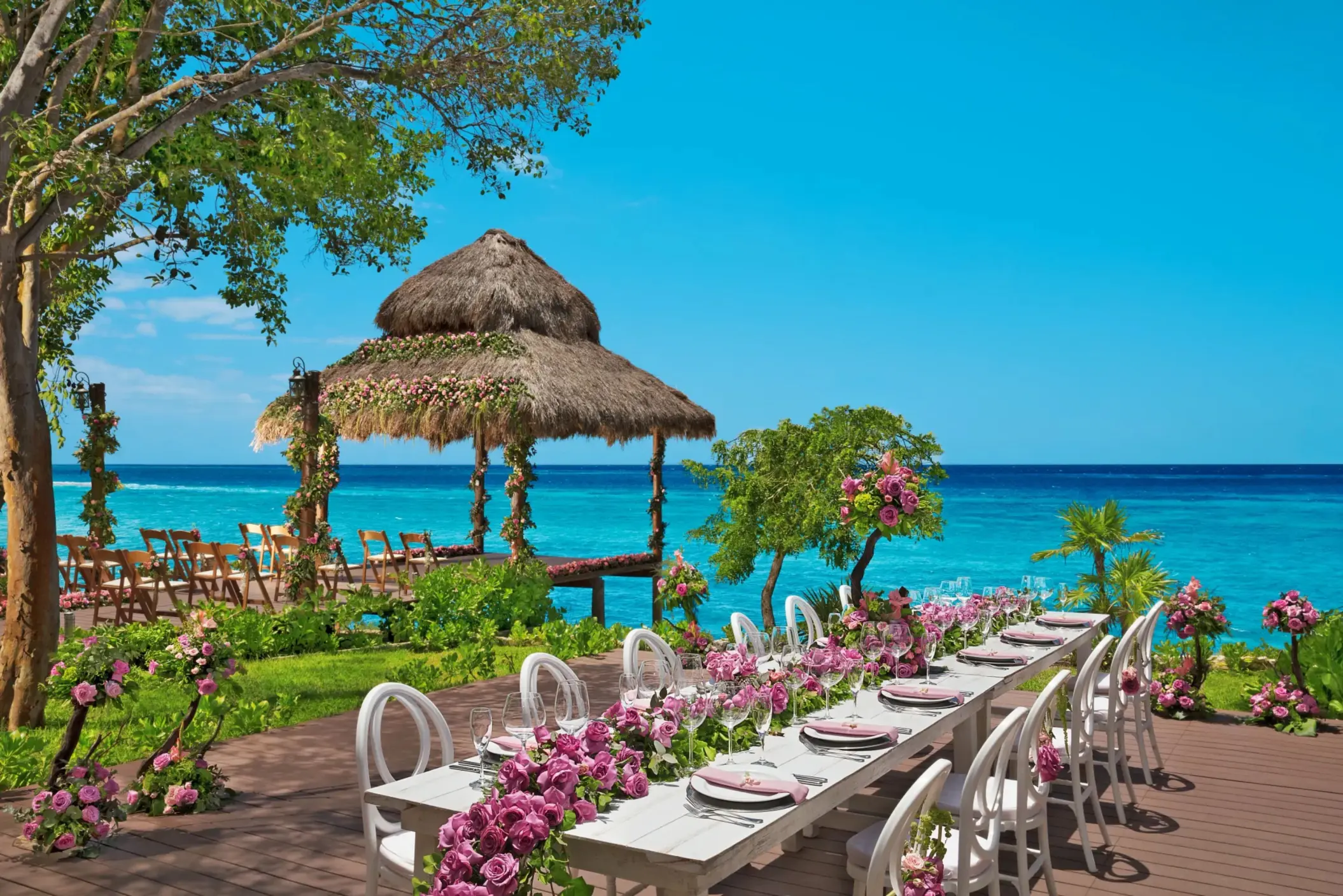 Oceanfront gazebo wedding reception setup with long floral table and turquoise sea backdrop.