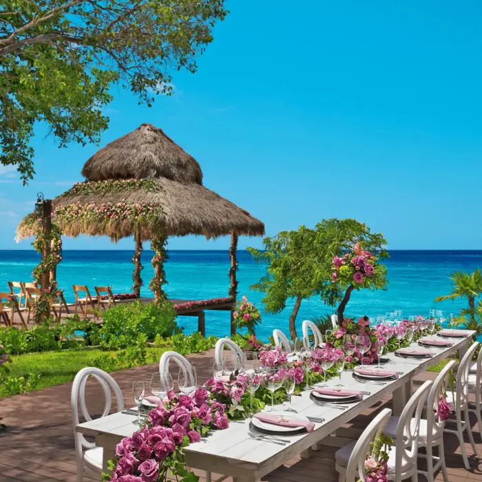 Oceanfront gazebo wedding reception setup with long floral table and turquoise sea backdrop.