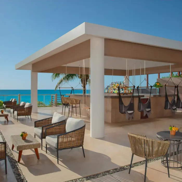 Modern beachfront rooftop bar with wicker furniture, hanging swing chairs, ocean views, and tropical setting