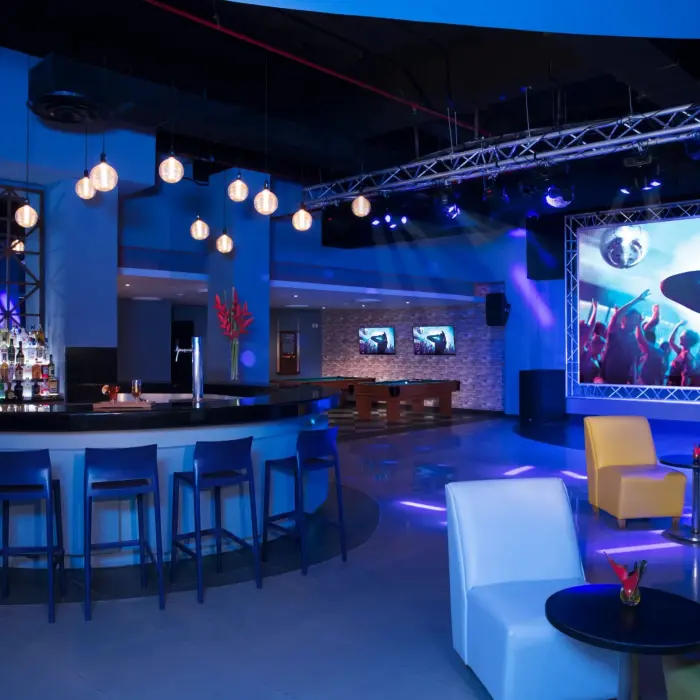 Contemporary nightclub interior with blue lighting, projection screens, bar seating, and modern lounge furniture