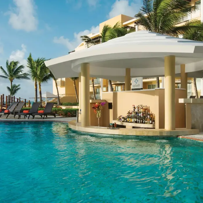 Tropical resort swim-up pool bar with circular design, palm trees, and guests relaxing on poolside loungers.