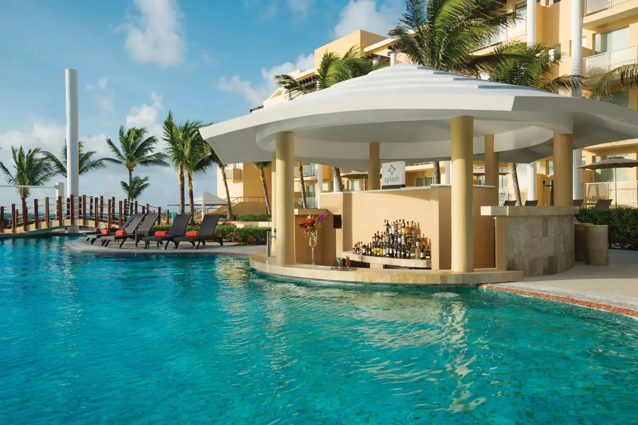 Tropical resort swim-up pool bar with circular design, palm trees, and guests relaxing on poolside loungers.