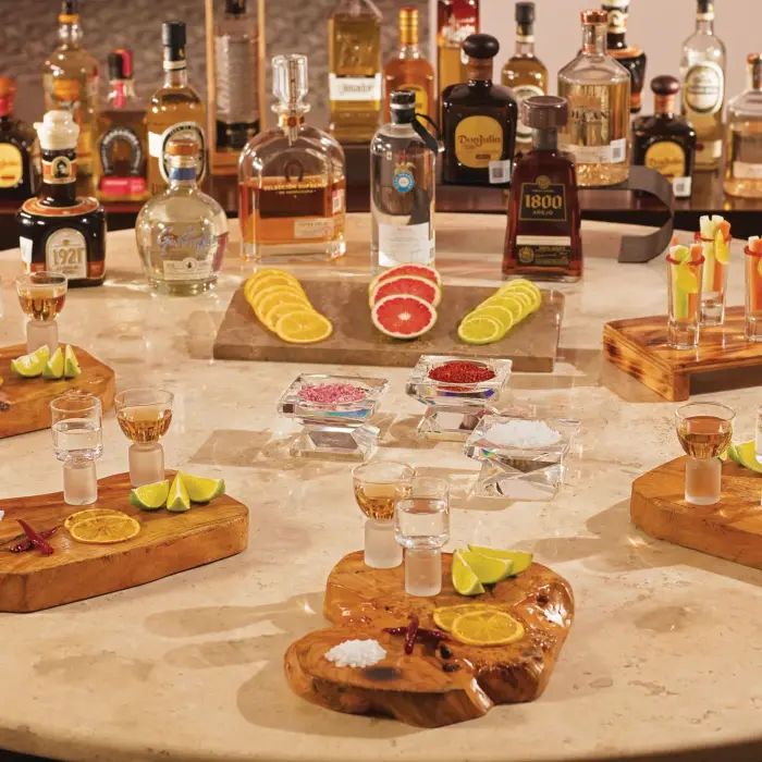 Premium tequila tasting setup with multiple bottles, wooden serving boards, citrus garnishes, and shot glasses.