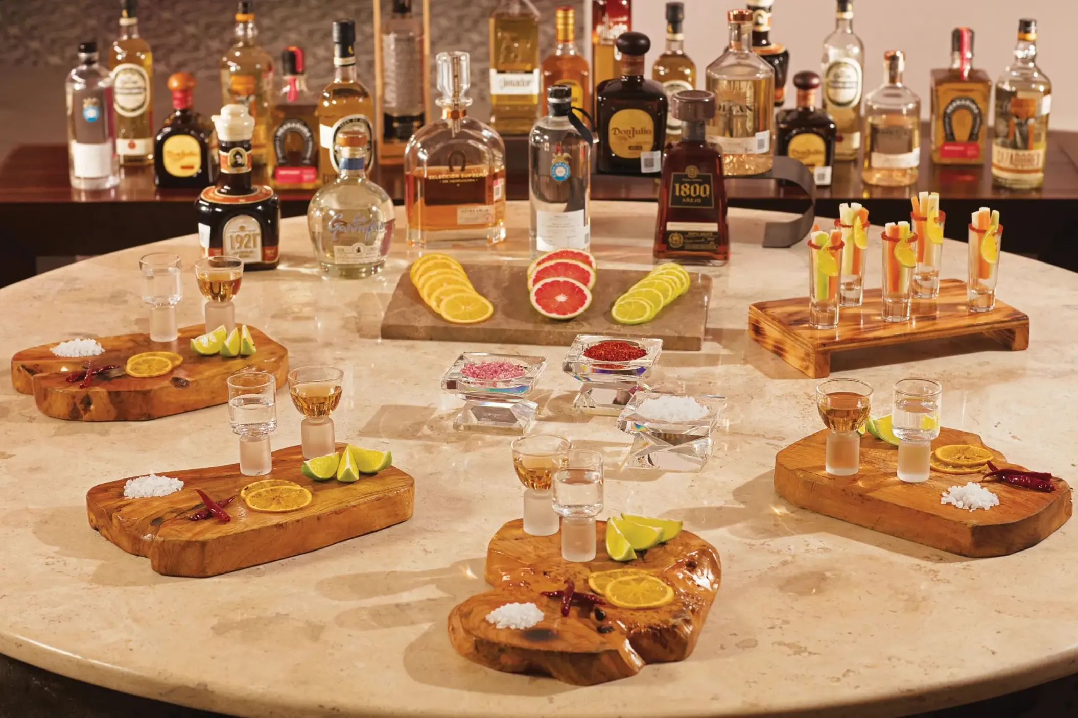 Premium tequila tasting setup with multiple bottles, wooden serving boards, citrus garnishes, and shot glasses.