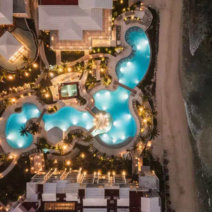 Nighttime aerial view of resort pools and beachfront with glowing lights highlighting the elegant layout.