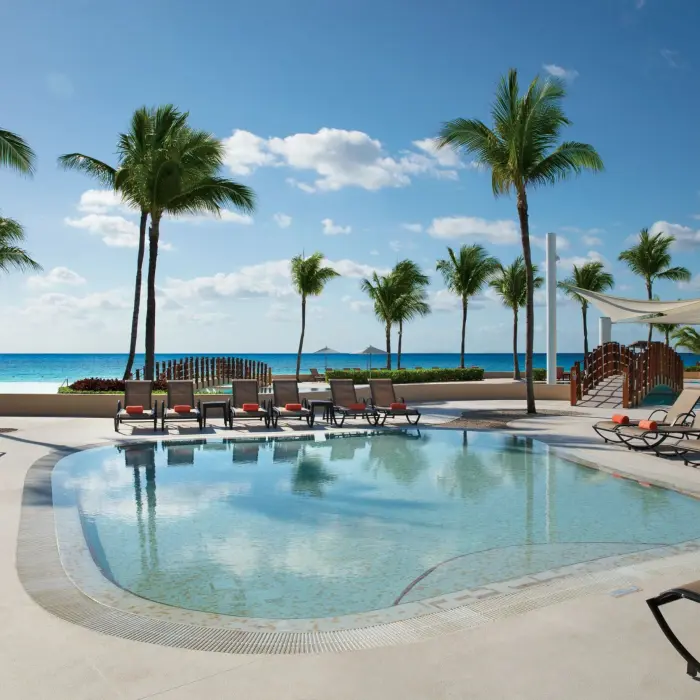 Kid-friendly pool with shallow waters, lounge chairs, and palm trees overlooking the ocean on a sunny day.