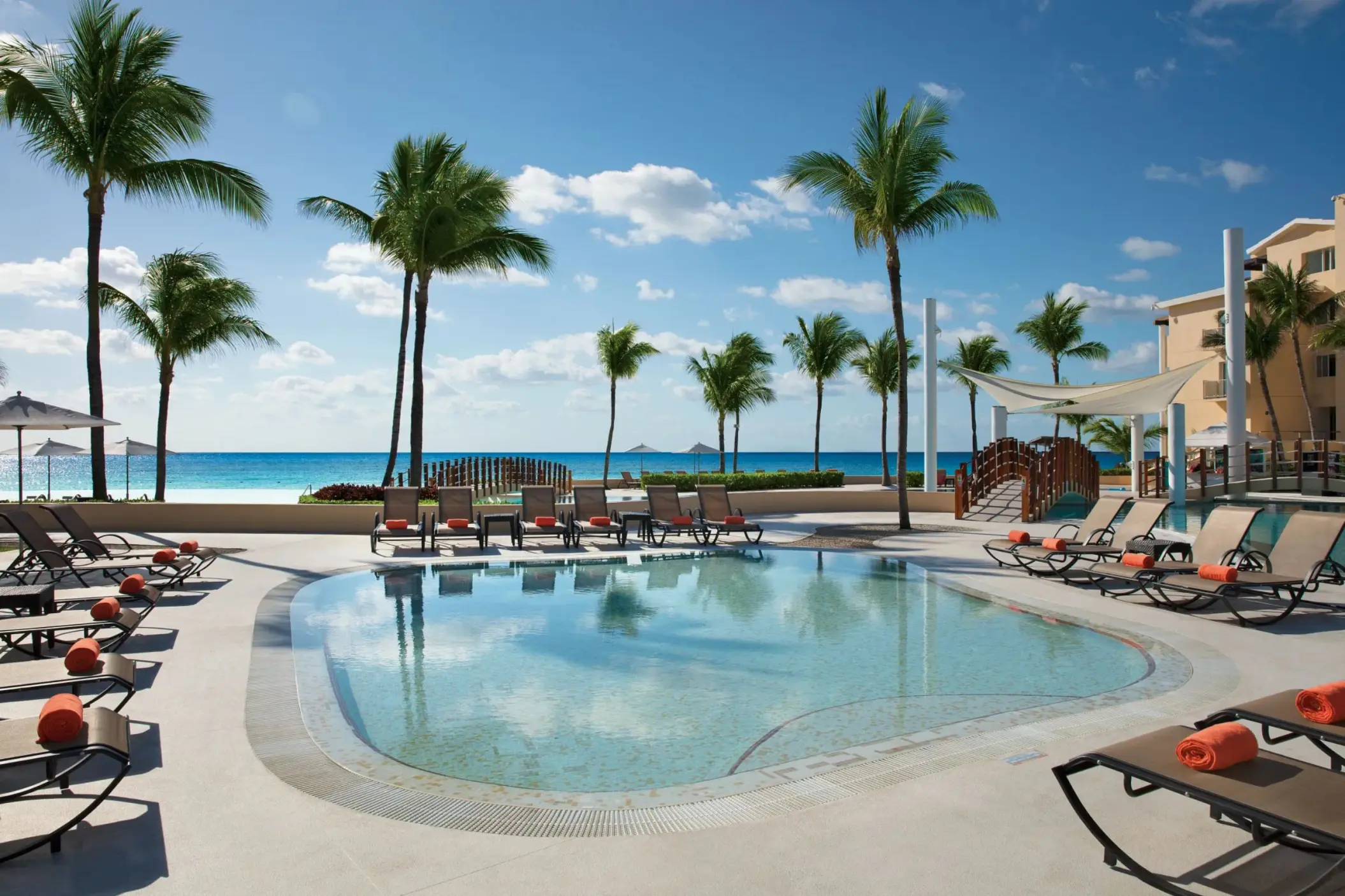 Kid-friendly pool with shallow waters, lounge chairs, and palm trees overlooking the ocean on a sunny day.