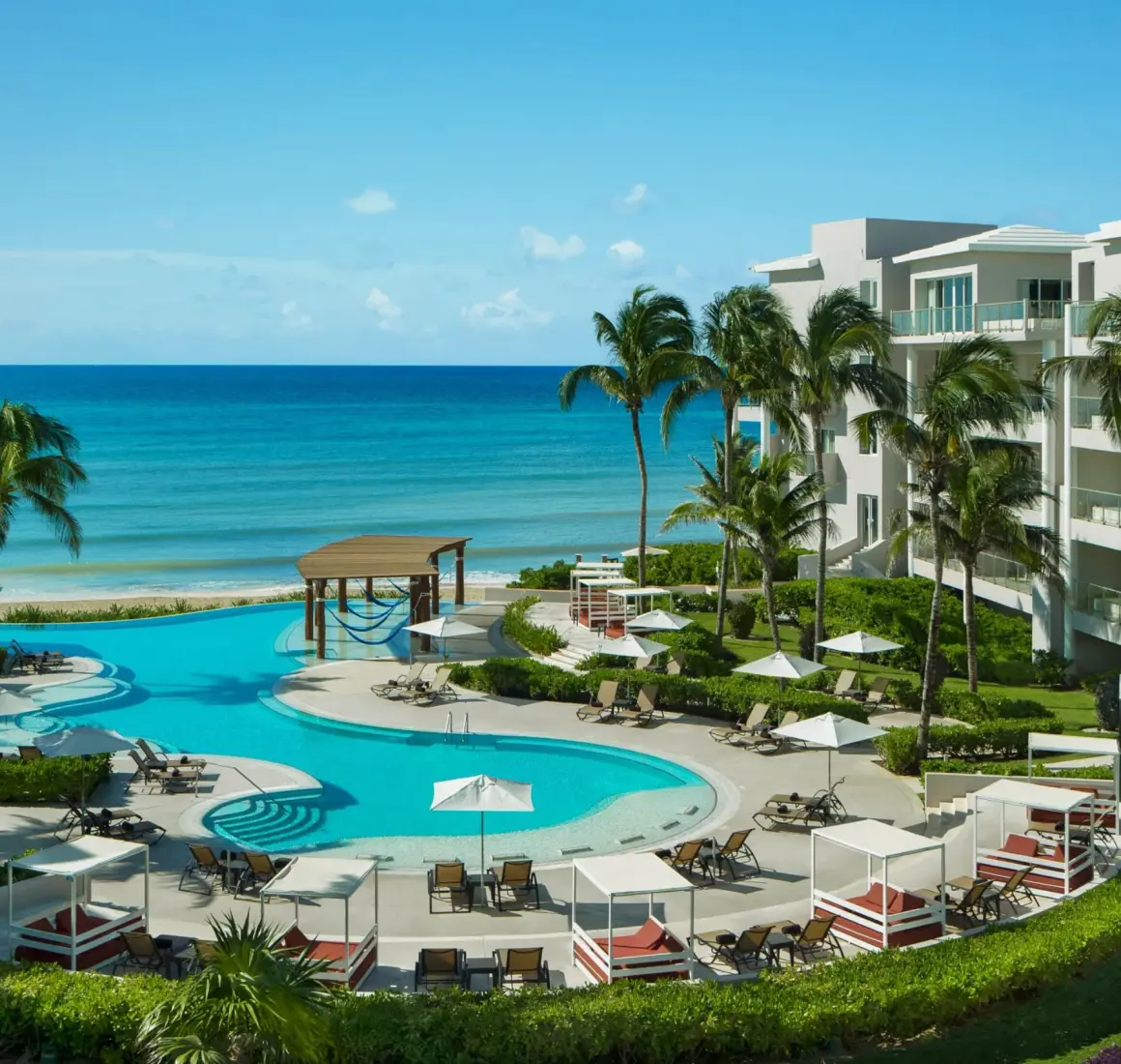 Serene adults-only pool area surrounded by palm trees, daybeds, and a scenic view of the Caribbean Sea.