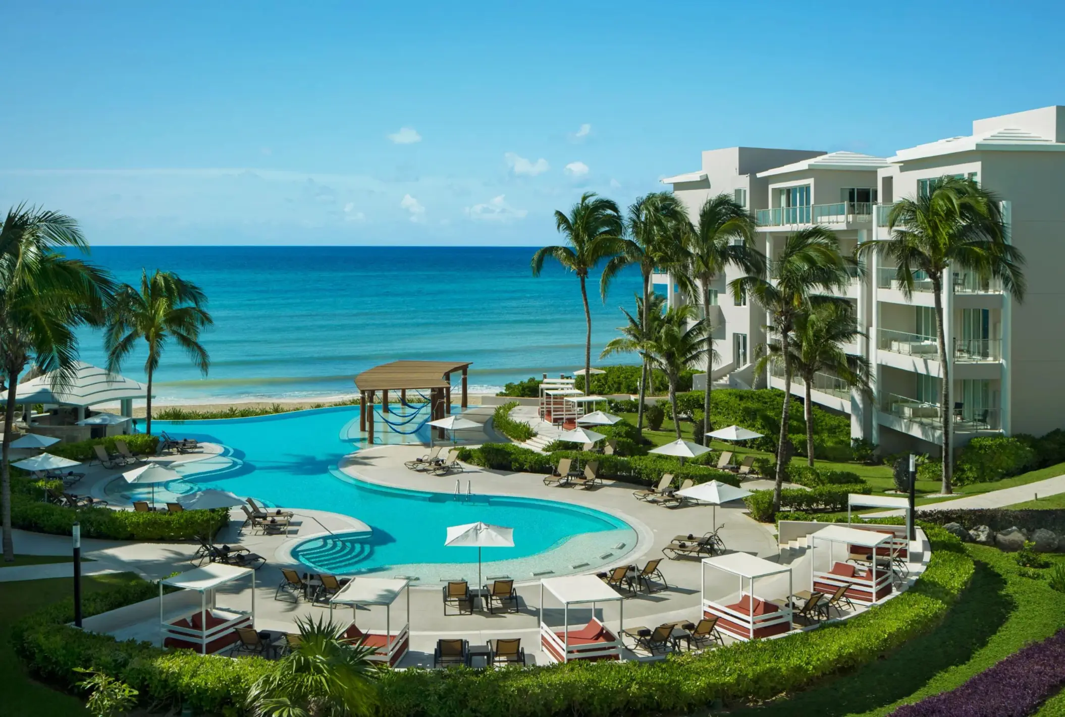 Serene adults-only pool area surrounded by palm trees, daybeds, and a scenic view of the Caribbean Sea.