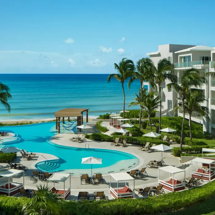 Serene adults-only pool area surrounded by palm trees, daybeds, and a scenic view of the Caribbean Sea.