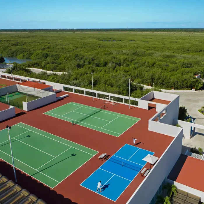 Rooftop sports complex with tennis, pickleball, and soccer courts surrounded by lush greenery and blue skies.