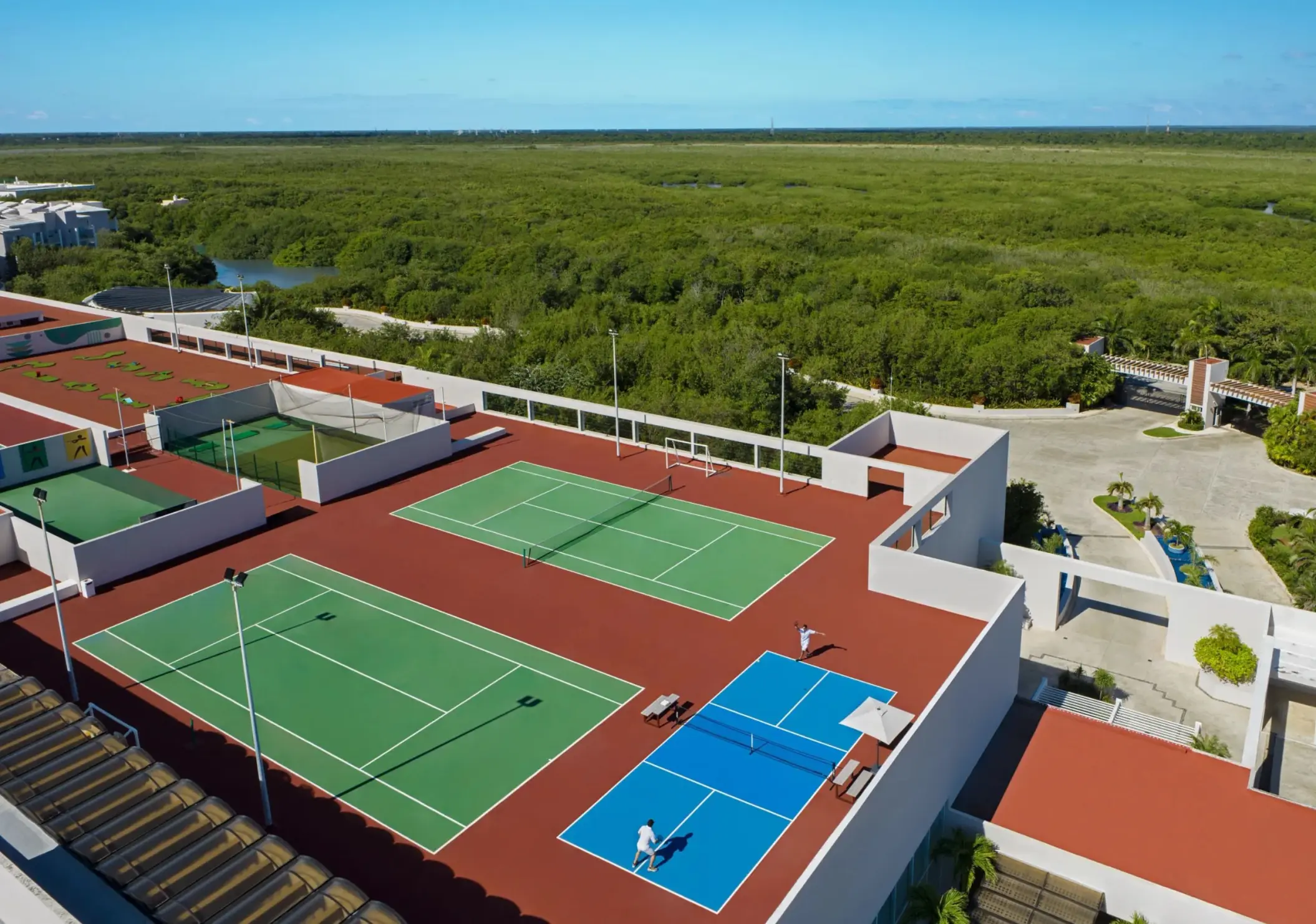 Rooftop sports complex with tennis, pickleball, and soccer courts surrounded by lush greenery and blue skies.