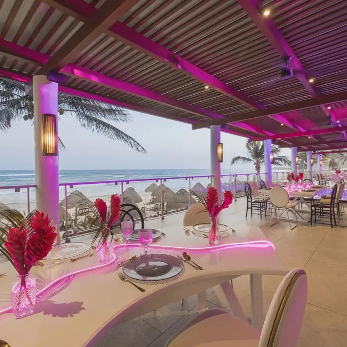 Open-air restaurant terrace with sweeping beach views, purple ambient lighting, and modern dining setup.
