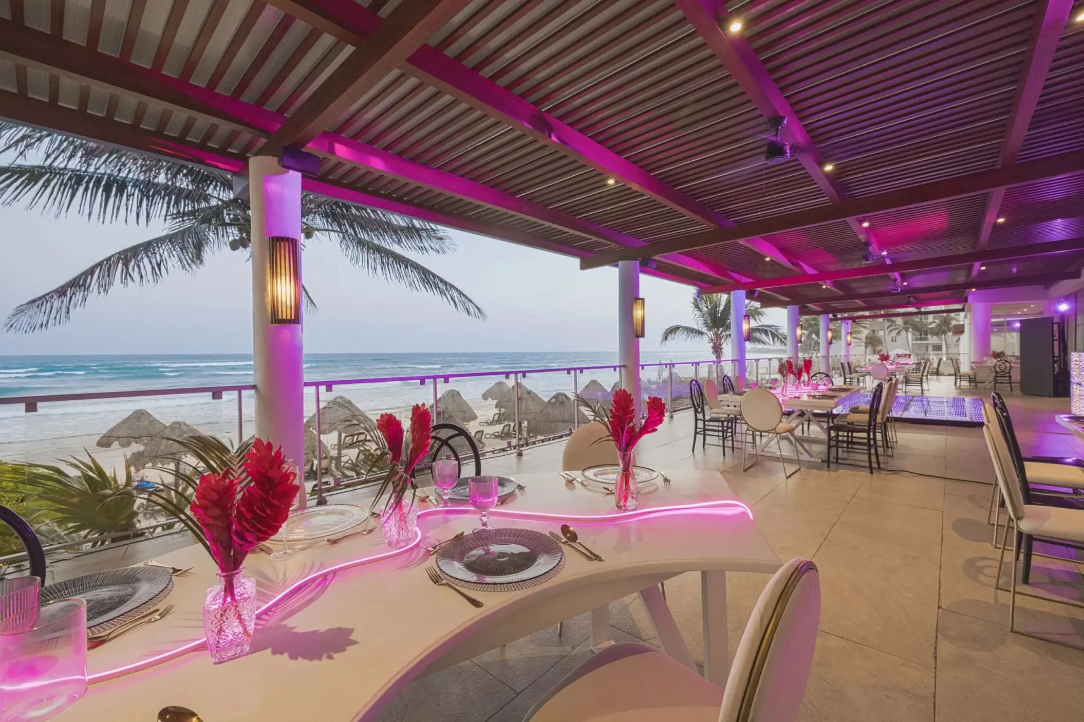 Open-air restaurant terrace with sweeping beach views, purple ambient lighting, and modern dining setup.