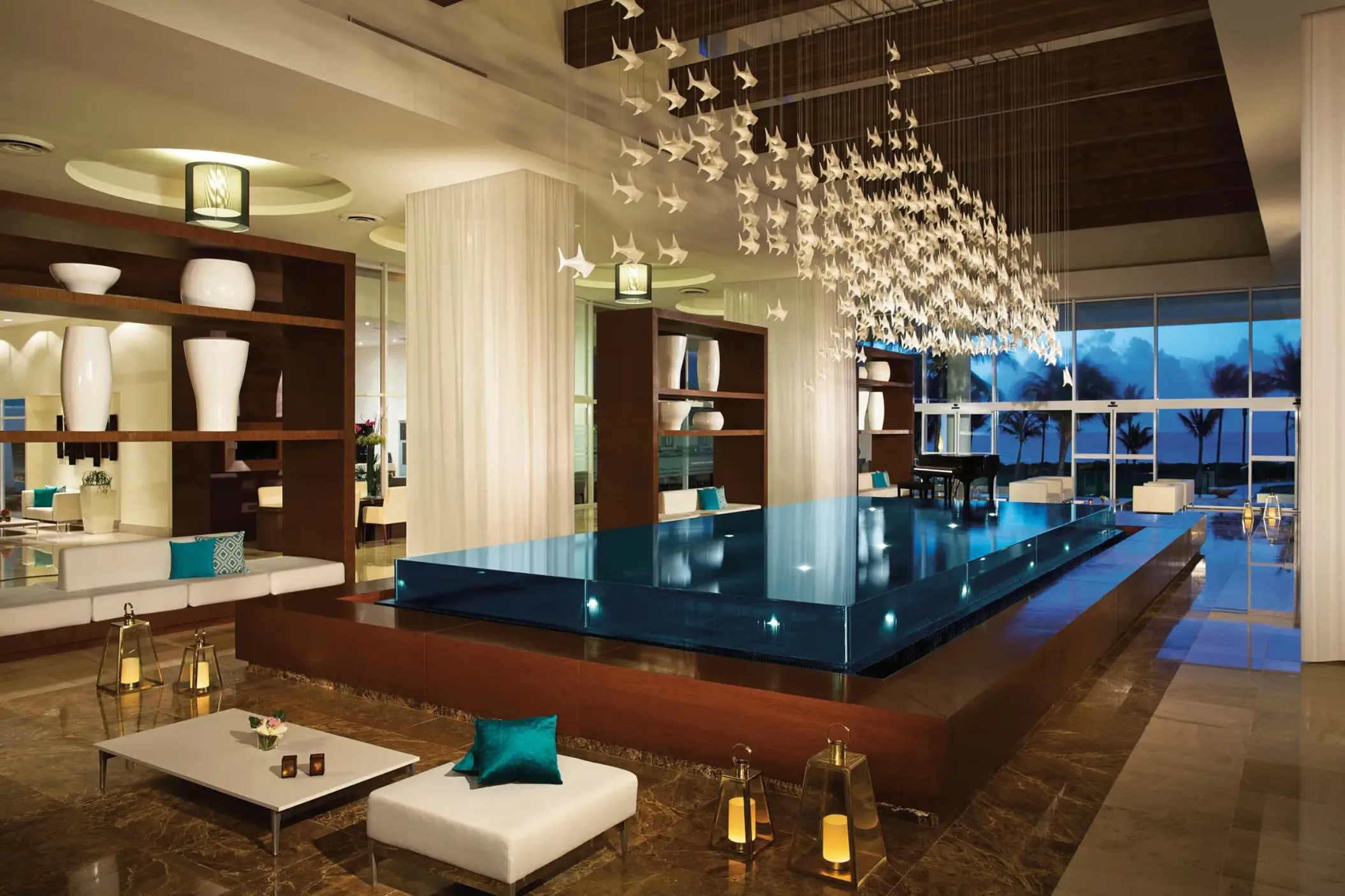 Modern lobby with chic seating, floating platform, lanterns, and ceiling installation of white hanging birds.