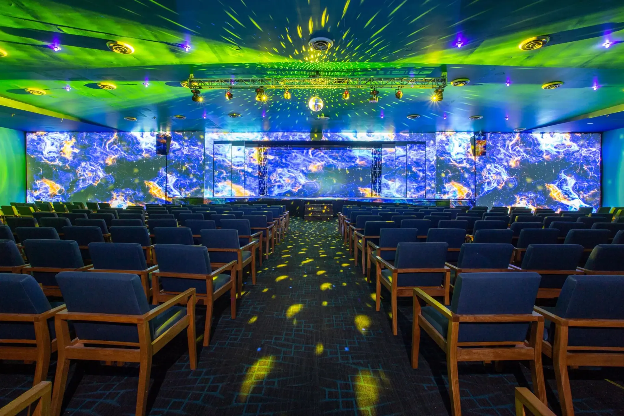 Colorful indoor theater with tiered seating, a vibrant LED stage, and dazzling lighting for immersive entertainment.