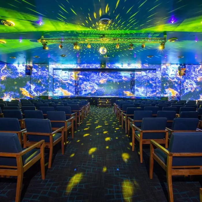 Colorful indoor theater with tiered seating, a vibrant LED stage, and dazzling lighting for immersive entertainment.