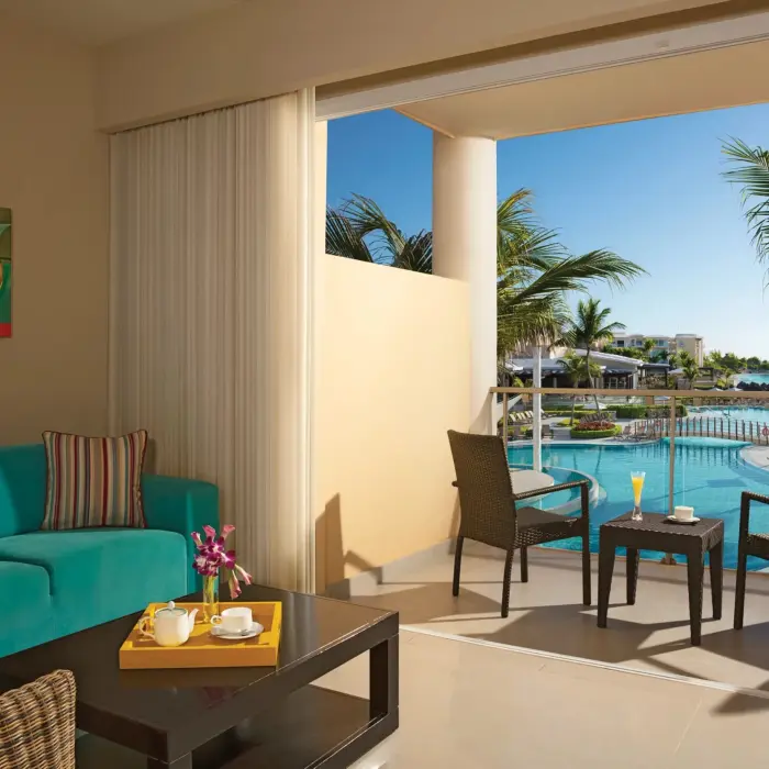 Junior suite balcony view with teal sofa and tropical drinks overlooking the pool and resort landscape.
