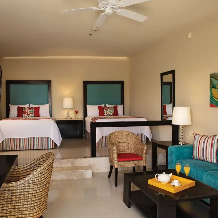 Cozy junior suite with two double beds, vibrant accent pillows, and a small sitting area with tropical decor.