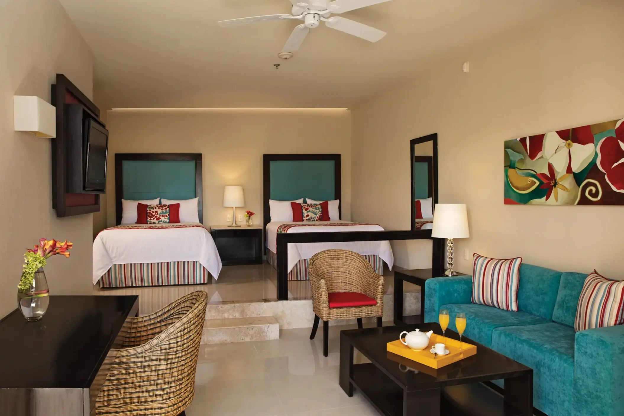 Cozy junior suite with two double beds, vibrant accent pillows, and a small sitting area with tropical decor.