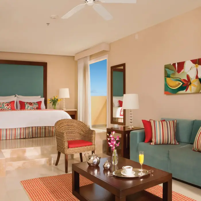 Spacious junior suite with king bed, striped accents, sitting area, and balcony with ocean glimpses.