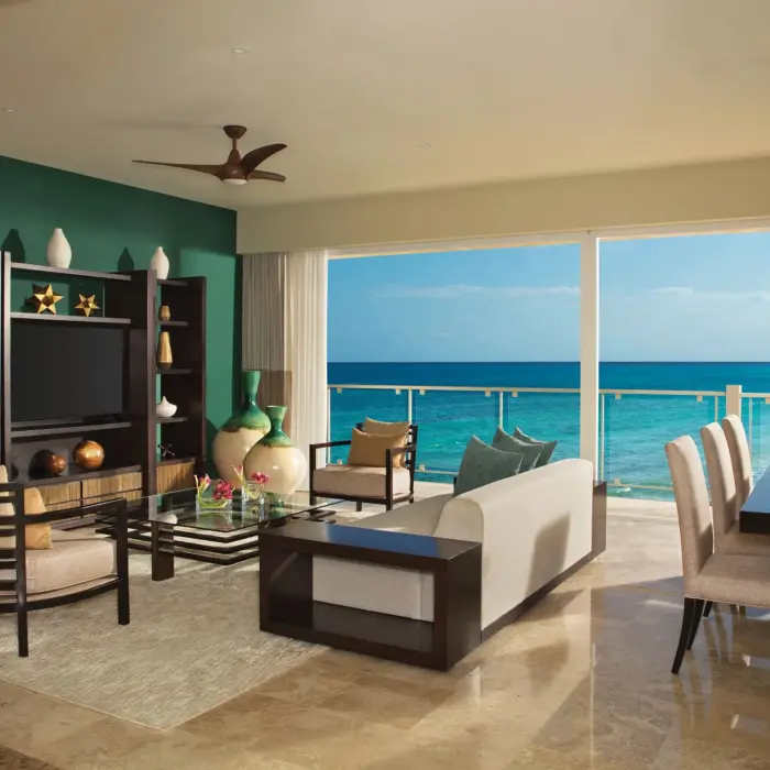 Spacious oceanfront living and dining area with modern decor, full wall window, and views of the Caribbean Sea.