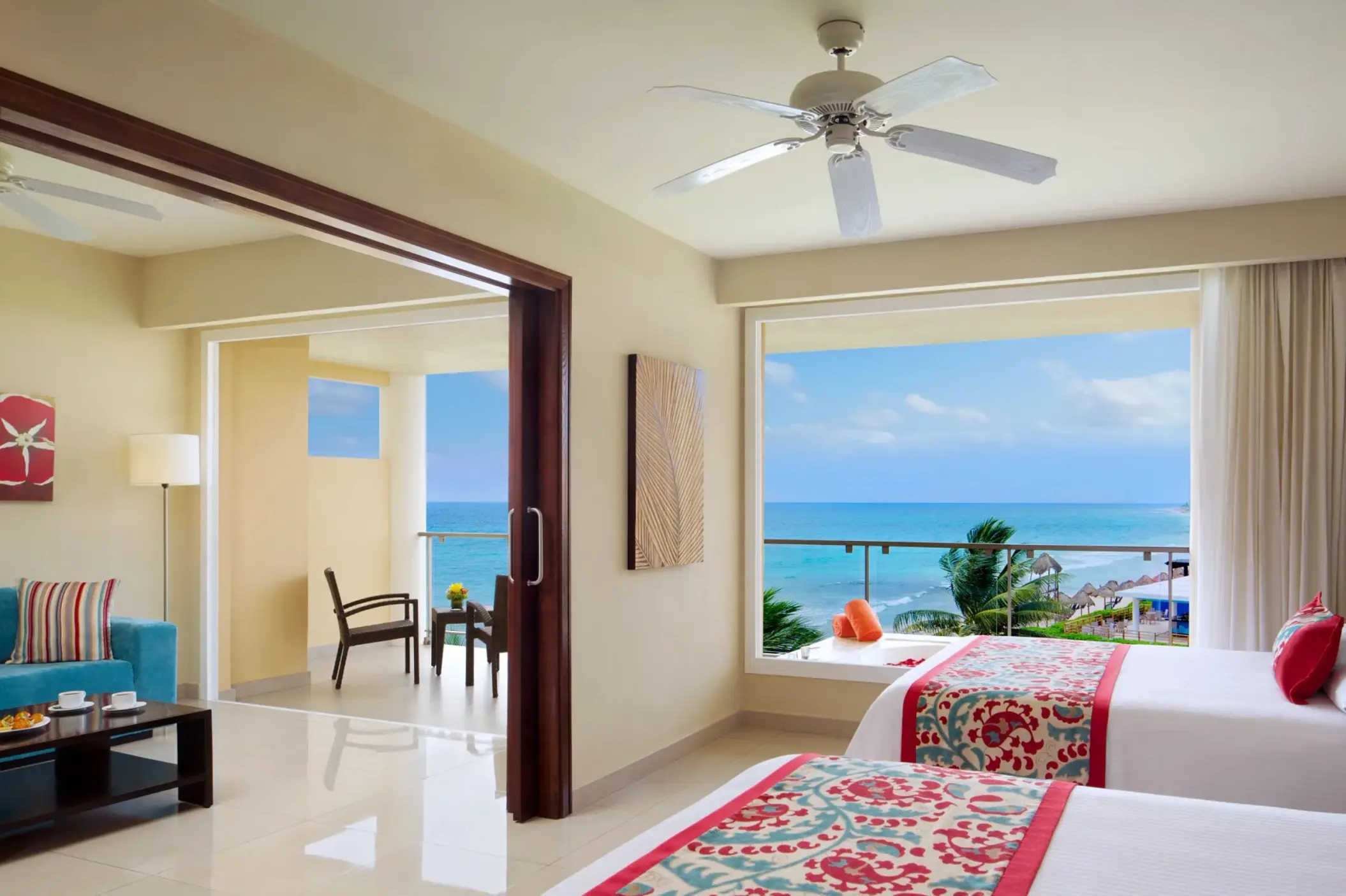 Bright oceanview suite with two beds, sitting area, and panoramic windows overlooking turquoise waters.