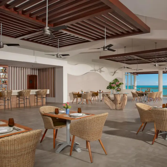 Casual oceanfront restaurant with rattan furniture, ceiling fans, and a spacious open design.