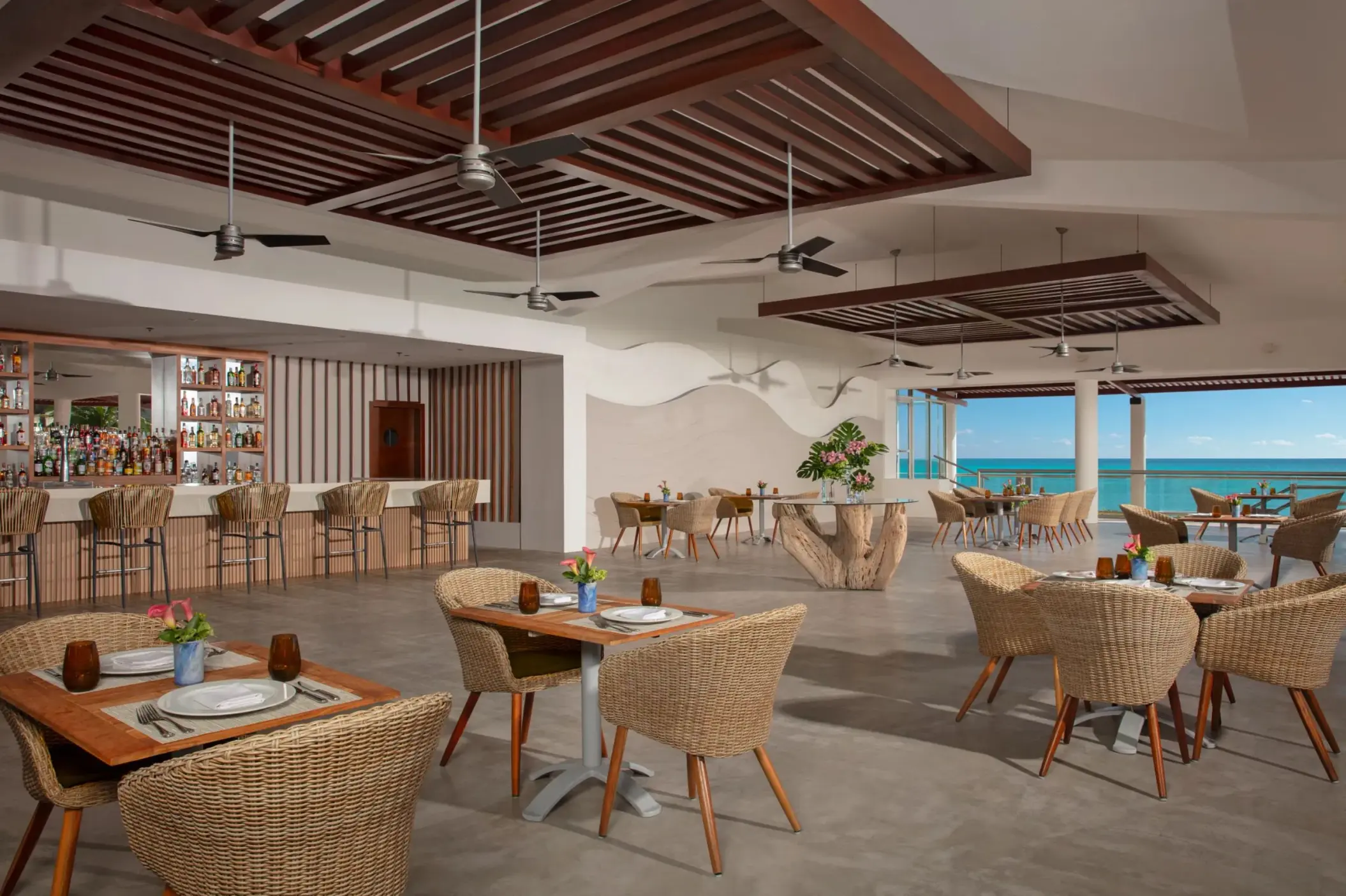 Casual oceanfront restaurant with rattan furniture, ceiling fans, and a spacious open design.