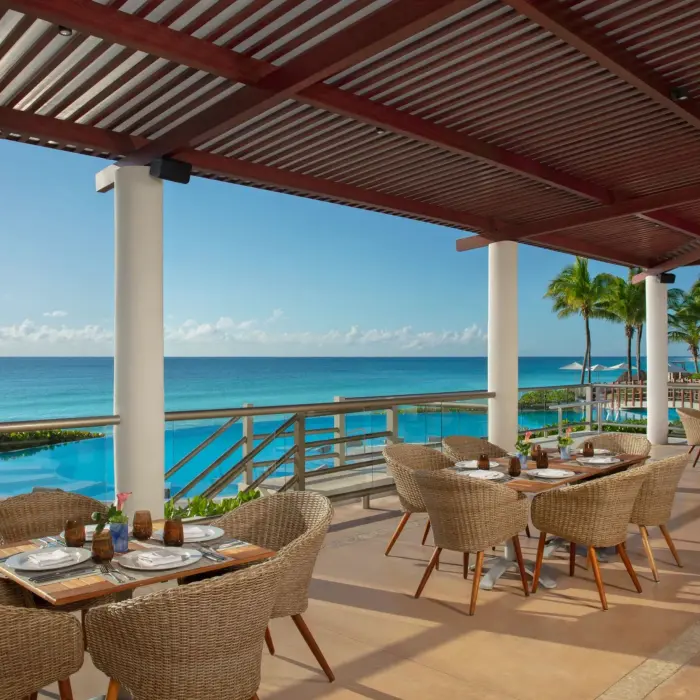 Open-air restaurant terrace with woven chairs and panoramic views of the pool and ocean beyond.