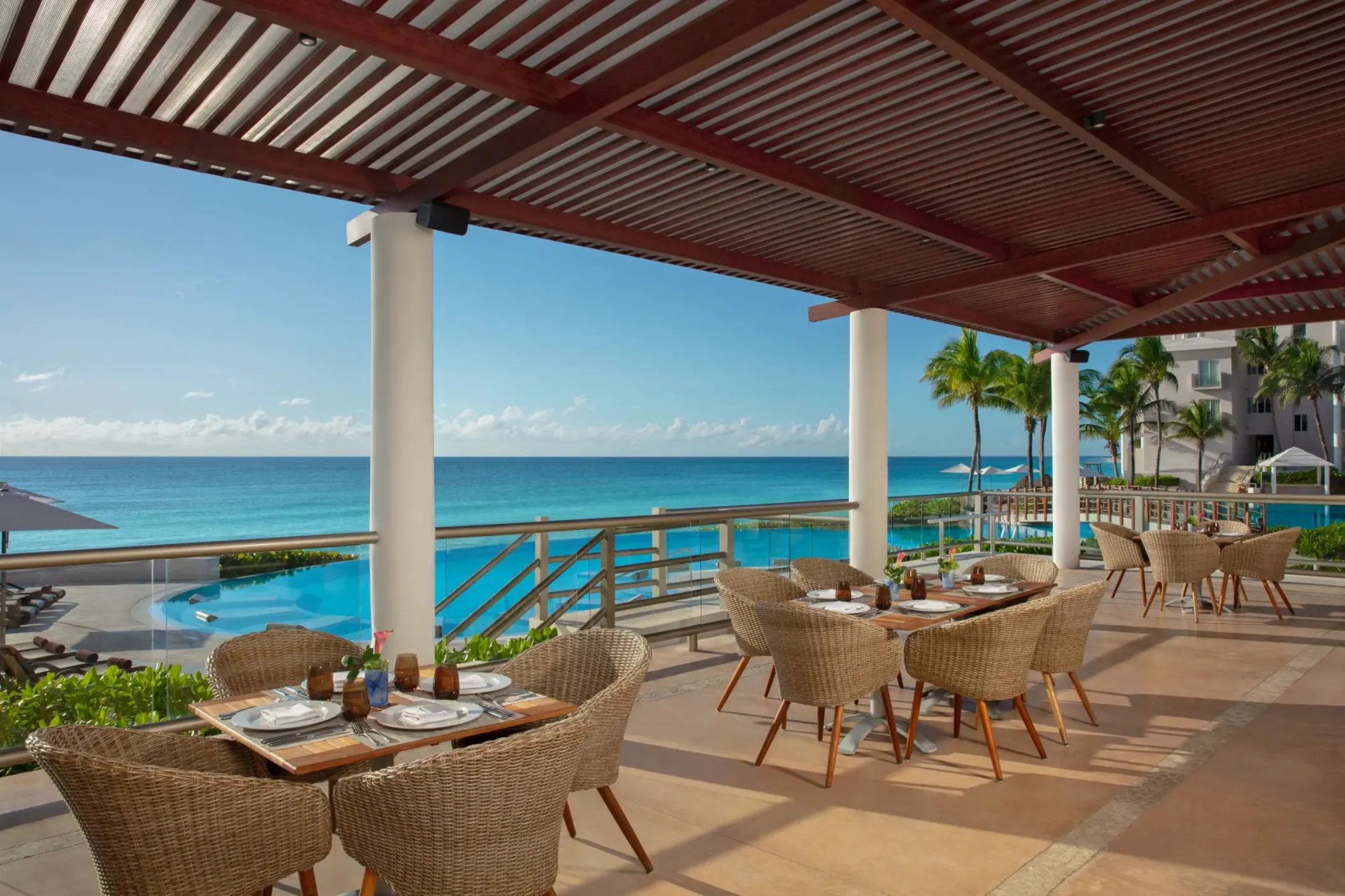 Open-air restaurant terrace with woven chairs and panoramic views of the pool and ocean beyond.