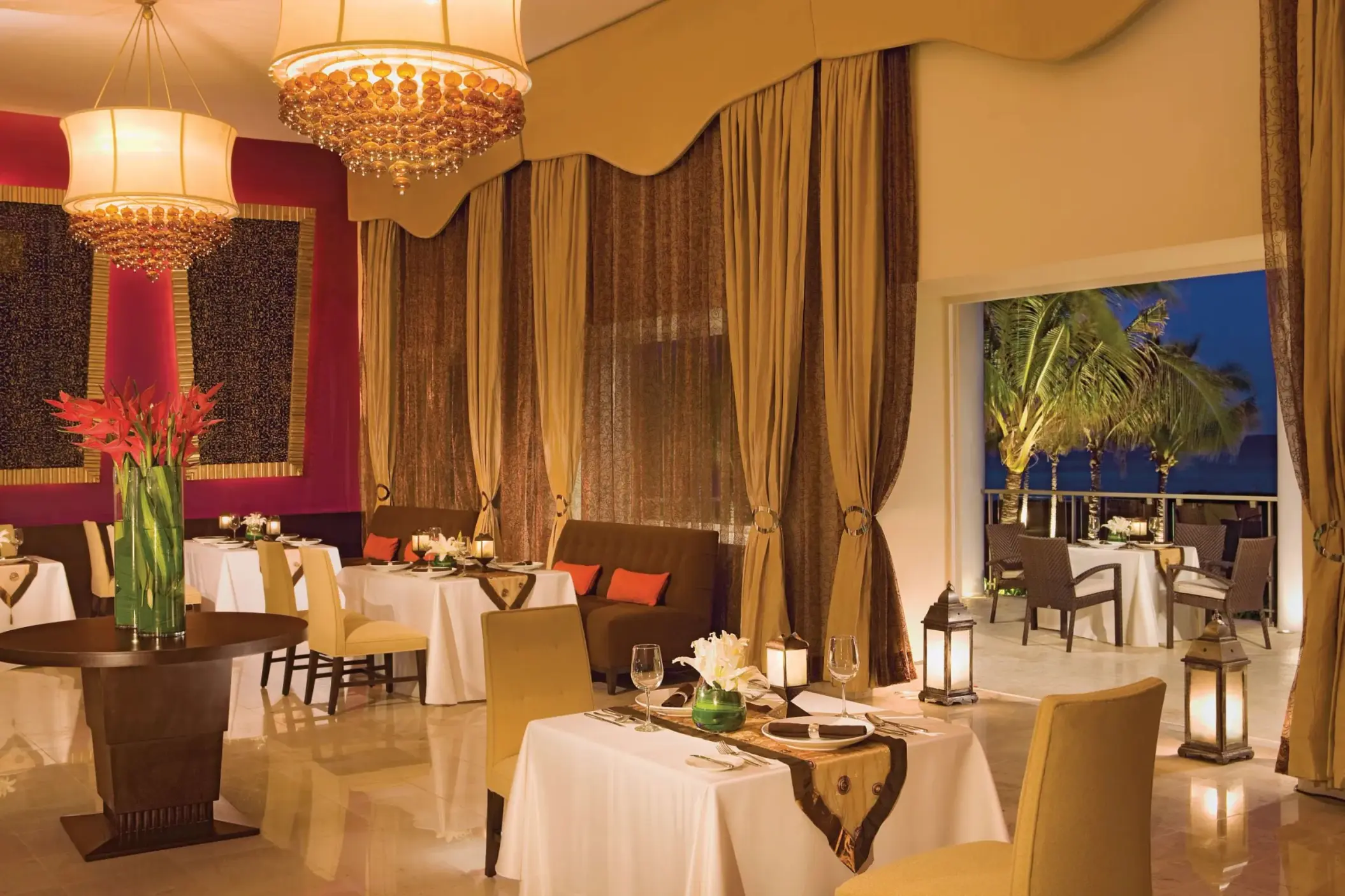 Elegant indoor dining room with crystal chandeliers, gold curtains, and tables set for romantic dinners.