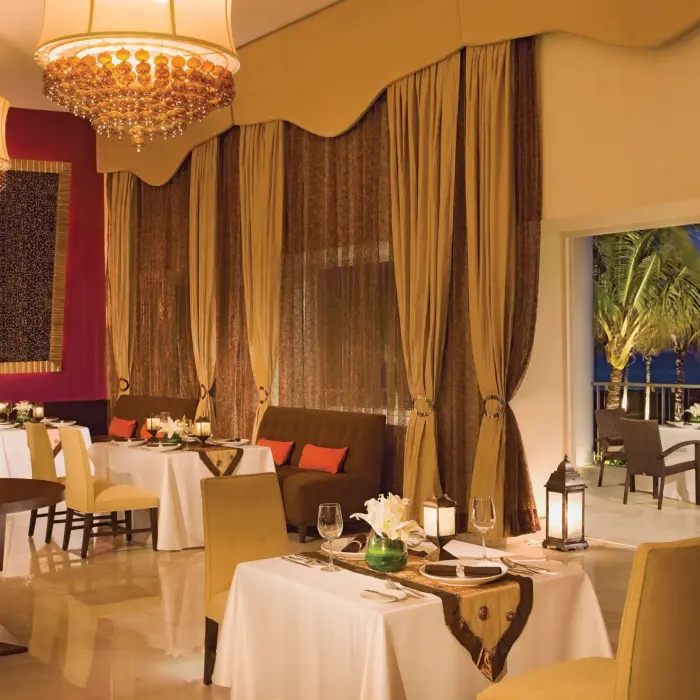 Elegant indoor dining room with crystal chandeliers, gold curtains, and tables set for romantic dinners.