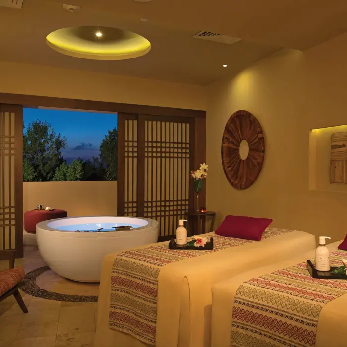 Elegant spa cabin with twin massage beds, wooden decor, and a private outdoor tub set against evening skies.