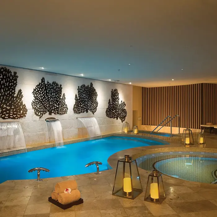 Indoor hydrotherapy circuit with cascading waterfalls, warm lighting, and lounge chairs by the spa pool.