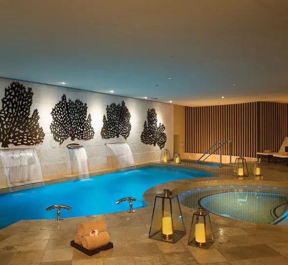 Indoor hydrotherapy circuit with cascading waterfalls, warm lighting, and lounge chairs by the spa pool.