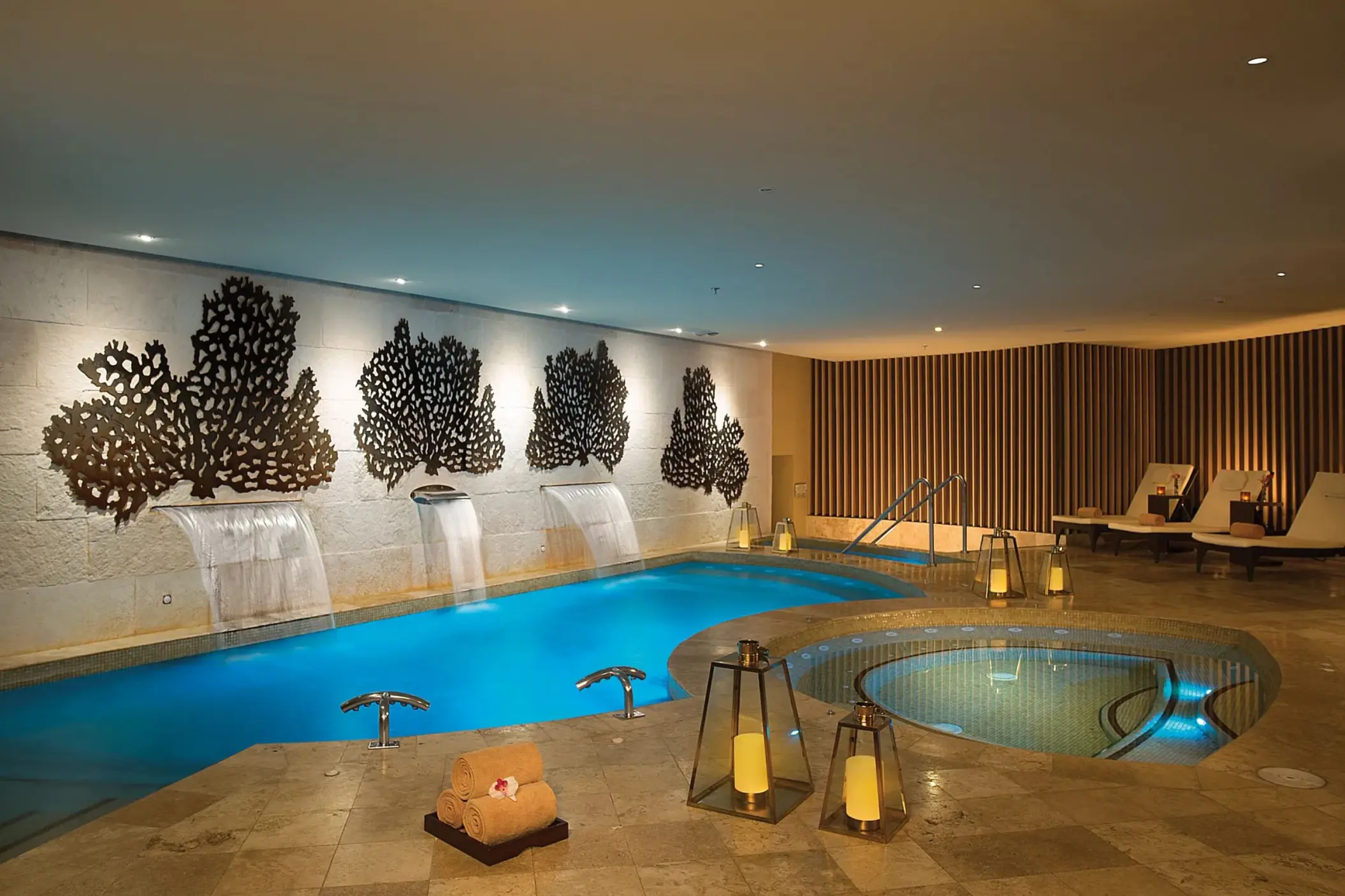 Indoor hydrotherapy circuit with cascading waterfalls, warm lighting, and lounge chairs by the spa pool.