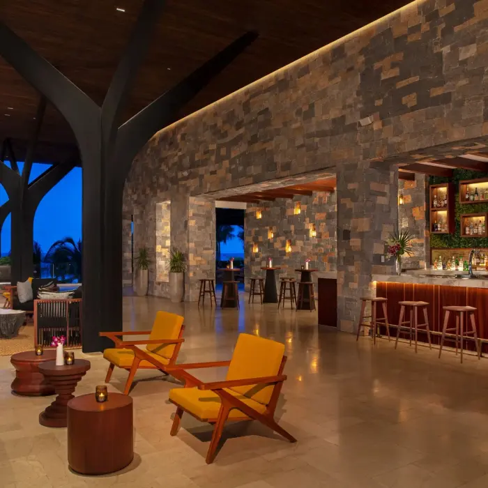 Elegant open-air bar with stone walls, warm lighting, and ocean views at night in Rendezvous Lounge.