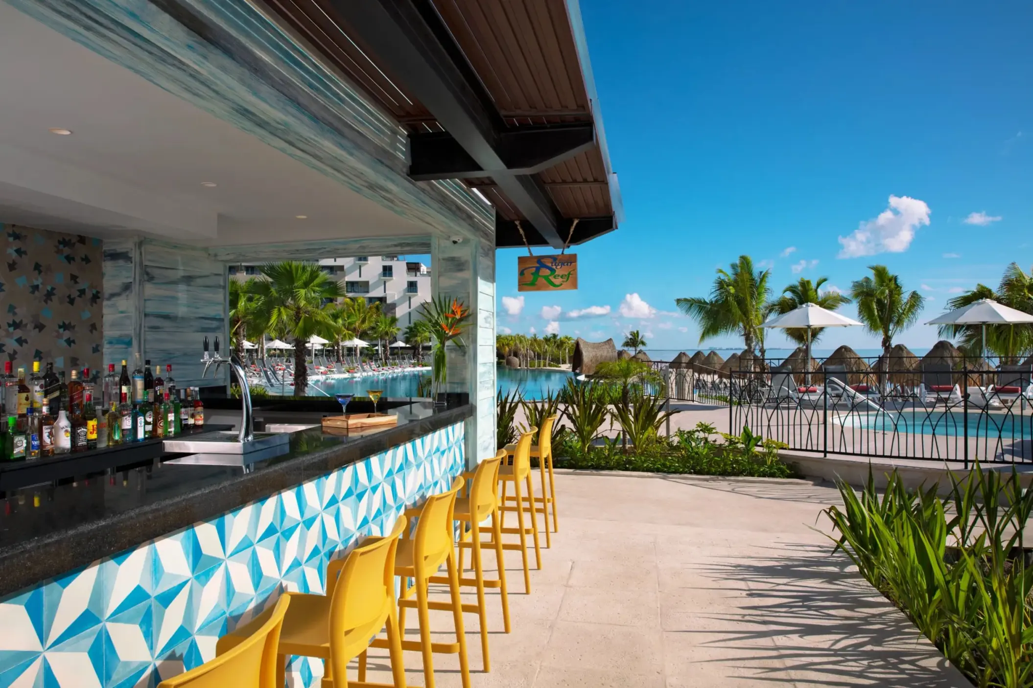 Outdoor poolside bar with bright yellow stools, tropical decor, and ocean views at Sugar Reef.