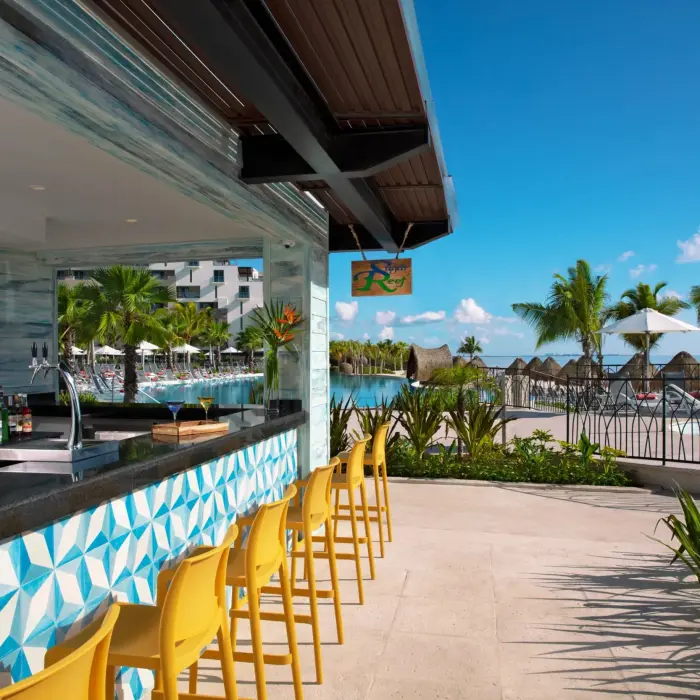 Outdoor poolside bar with bright yellow stools, tropical decor, and ocean views at Sugar Reef.