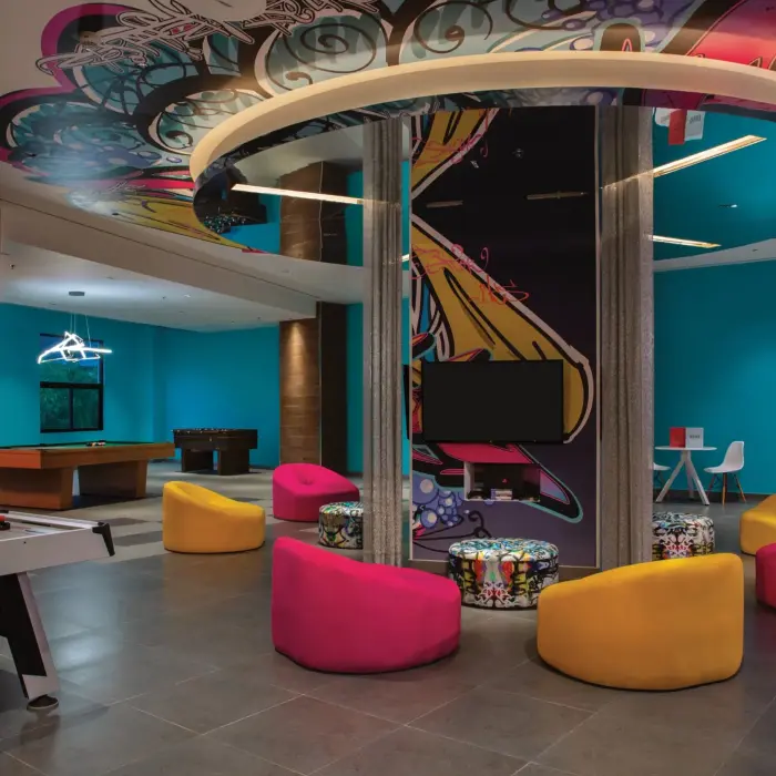 Vibrant teen club with colorful seating, arcade games, and bold graffiti art on the ceiling and central pillar.