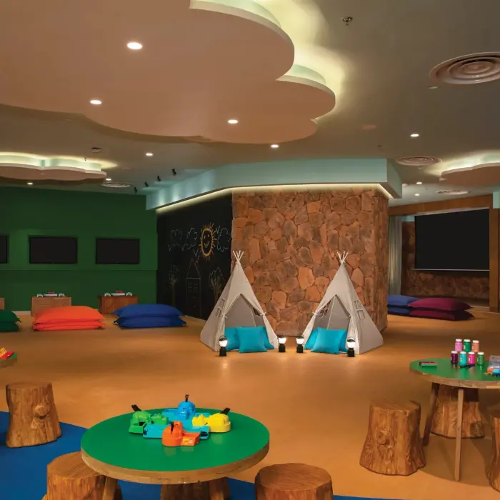 Kids’ indoor club with stone walls, teepees, game tables, and colorful floor cushions.