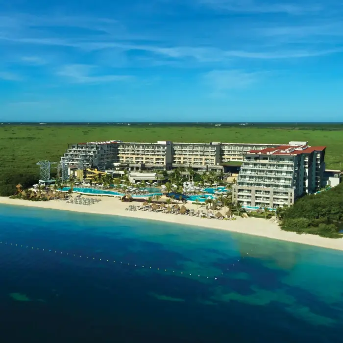 Aerial view of beachfront resort with pools and lush surroundings, bordered by turquoise Caribbean waters.