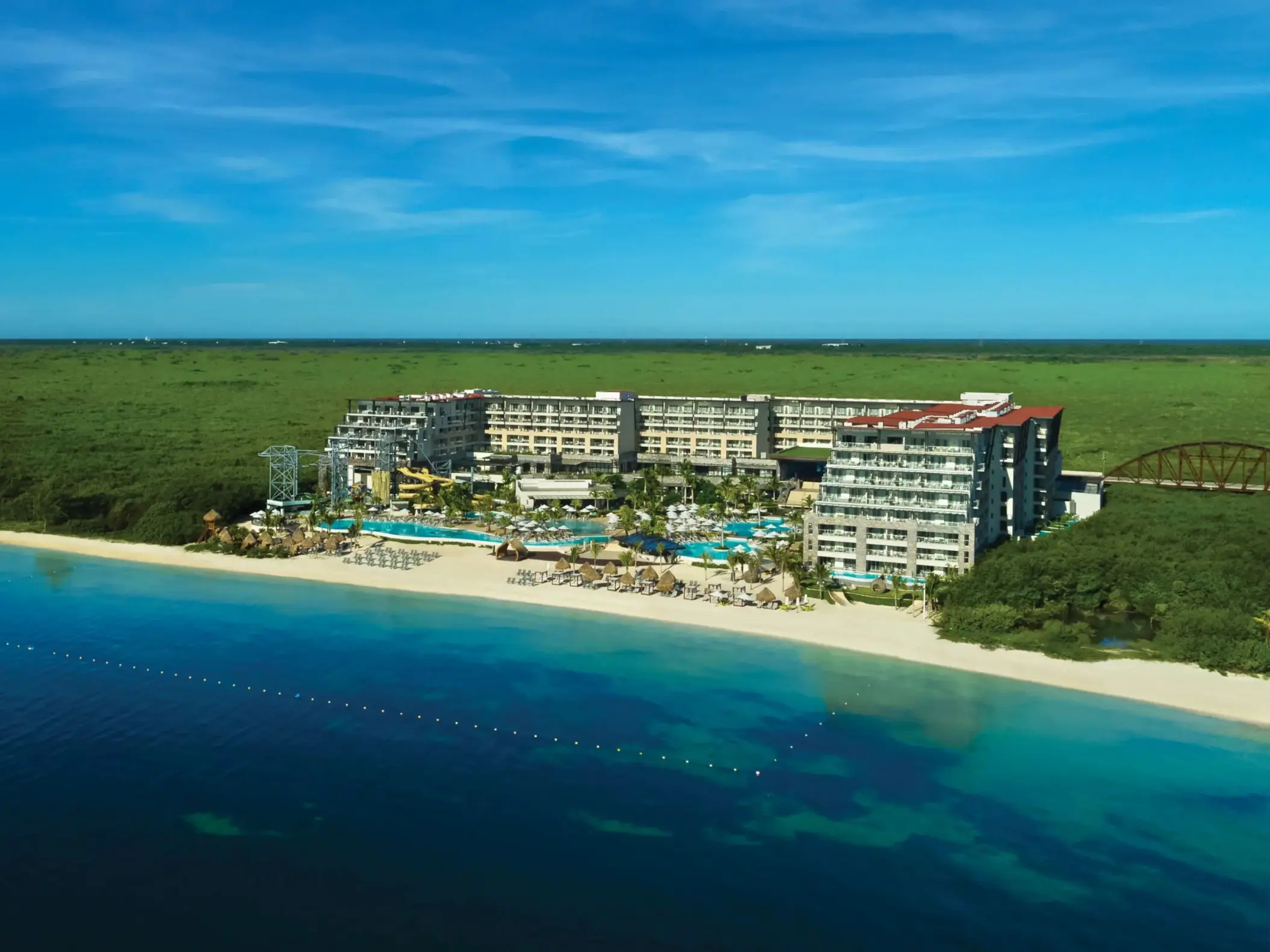 Aerial view of beachfront resort with pools and lush surroundings, bordered by turquoise Caribbean waters.