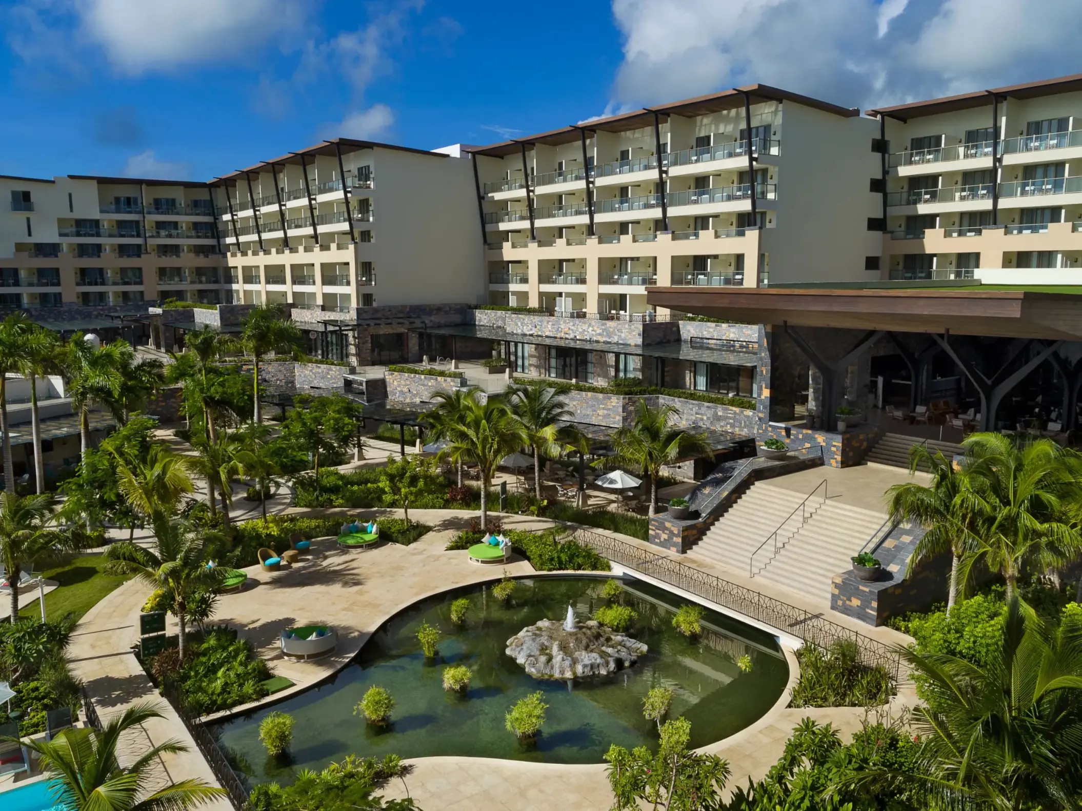Resort garden area with tropical landscaping, a central fishpond, and surrounding lush palm trees.